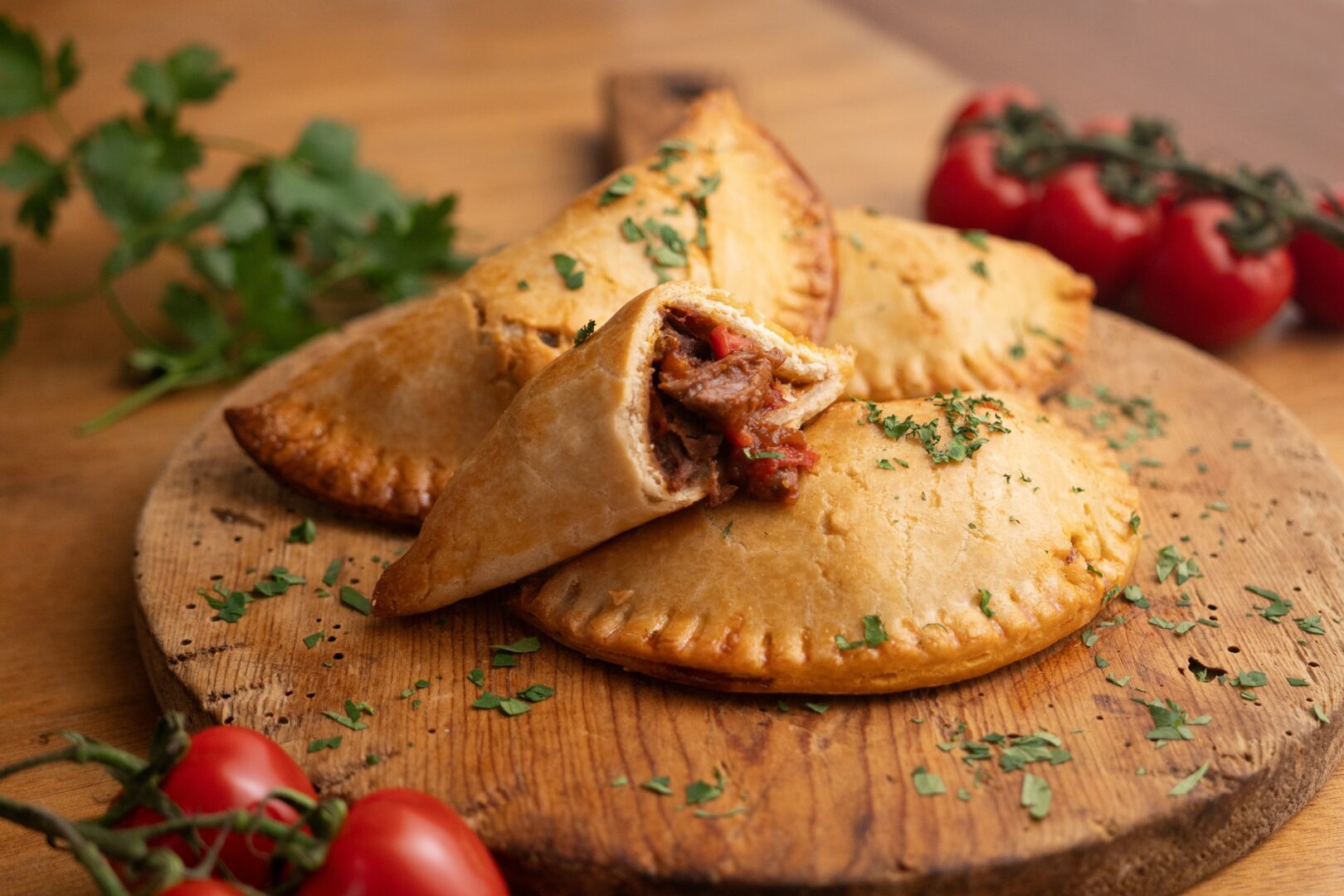 Argentinische Empanadas mit Rindfleisch, von Hand mit Tomaten auf einem Holzbrett zubereitet.